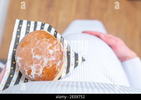 Schwangerschaft und ungesunde Ernährung Konzept: Schwangere Frau hält einen Teller mit leckeren Donuts in der Hand Stockfoto