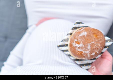 Schwangerschaft und ungesunde Ernährung Konzept: Schwangere Frau hält einen Teller mit leckeren Donuts in der Hand Stockfoto