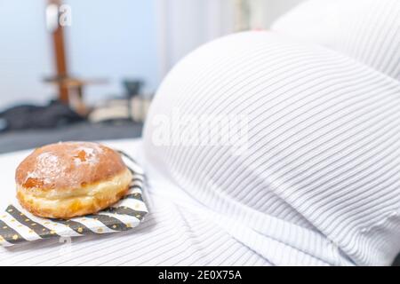 Schwangerschaft und ungesunde Ernährung Konzept: Schwangere Frau hält einen Teller mit leckeren Donuts in der Hand Stockfoto