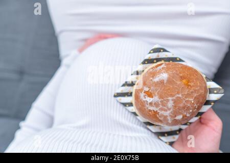 Schwangerschaft und ungesunde Ernährung Konzept: Schwangere Frau hält einen Teller mit leckeren Donuts in der Hand Stockfoto