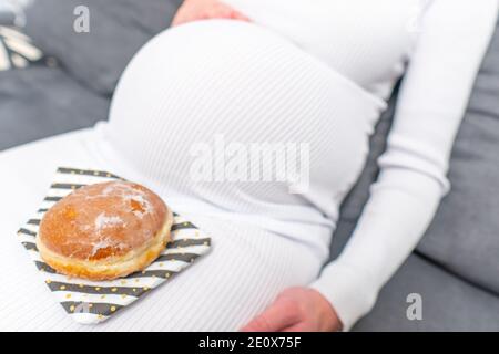 Schwangerschaft und ungesunde Ernährung Konzept: Schwangere Frau hält einen Teller mit leckeren Donuts in der Hand Stockfoto