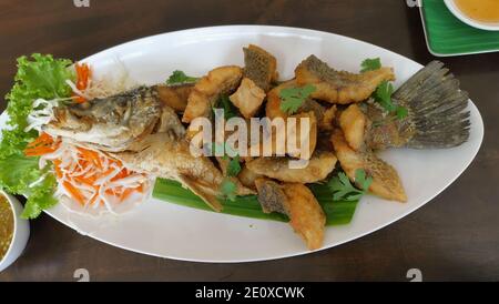 Gebratene Fischfilets die Schale mit dem Kopf und dem Fischbein anrichten. Tischset mit Bananenblättern auf weißem Teller. Thailändisches Essen. Stockfoto