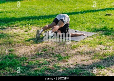 Junger sportlich schöner Mann, der Yoga im Park praktiziert und die Pflug-Pose macht. Stockfoto