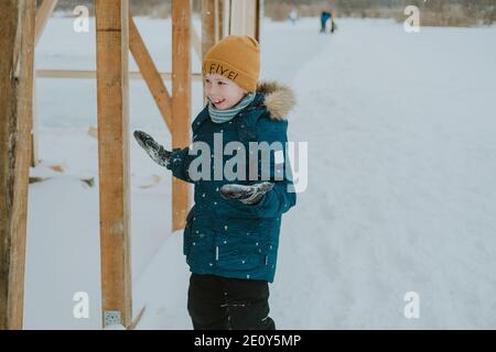 Winterspiele im Freien. Kinder spielen Schneebälle. Fröhlicher Junge, der im Winter draußen spielt. Winterurlaub für Kinder. Winterwanderungen. Stockfoto