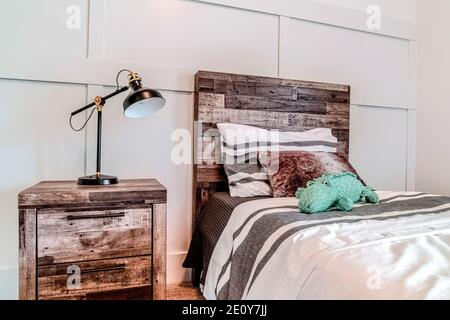 Lampe auf Beistelltisch neben dem Bett mit Holzkopfteil gegen Getäfelte Wand Stockfoto