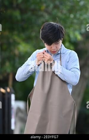 Porträt eines glücklichen jungen asiatischen Mannes trägt eine braune Schürze in seinem Gartenhaus. Stockfoto