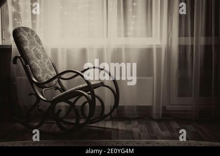 Im Abendlicht steht ein Schaukelstuhl am Fenster. Schwarze und weiße Sepia. Stockfoto