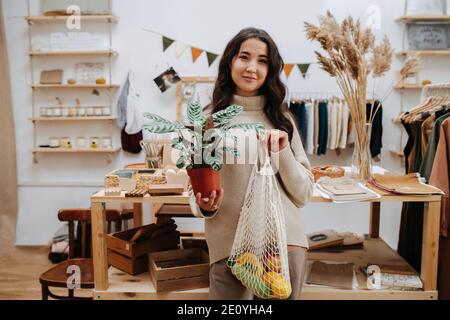 Porträt einer Frau im Öko-Shop posiert für ein Foto mit Netzbeutel und Topfpflanze Stockfoto