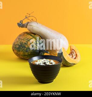 Vegetarische Cremesuppe mit rohen Kürbissen auf gelbem Hintergrund. Stockfoto