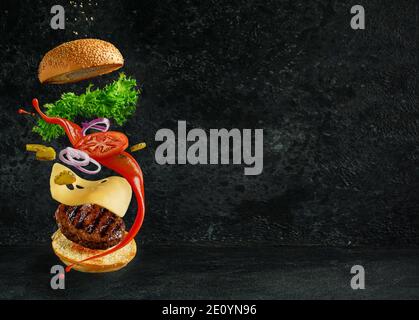 Hamburger mit schwebenden Zutaten auf dunklem Hintergrund. Kreatives Stillleben Konzept. Stockfoto