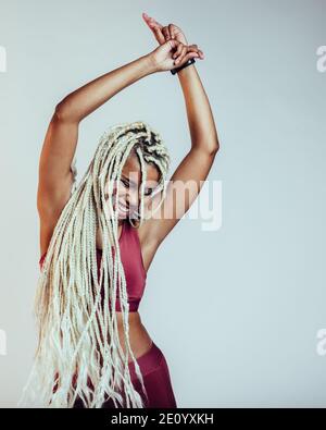 Porträt einer afroamerikanischen Fitness-Frau, die mit Händen in der Luft tanzt. Fröhliche Frau mit langen geflochtenen Haaren Spaß haben. Stockfoto