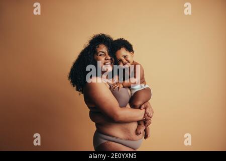 Porträt einer glücklichen Mutter mit ihrem Kind. Fröhliche Frau, die ihr Baby in den Armen trägt und die Kamera anschaut und lächelt. Stockfoto