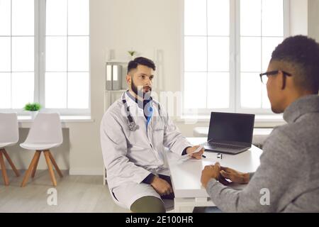 Männlicher Arzt erklärt die Ergebnisse einer medizinischen Untersuchung und Diagnostiziert seinen dunkelhäutigen Patienten Stockfoto