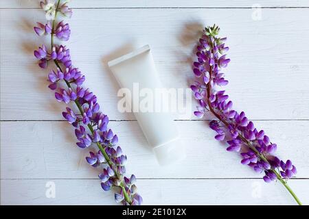 Mockup von nicht gebrandeten weißen Flaschenschlauch für Branding und lila Blumen auf weißem Holztisch mit horizontalen Brettern. Draufsicht Stockfoto