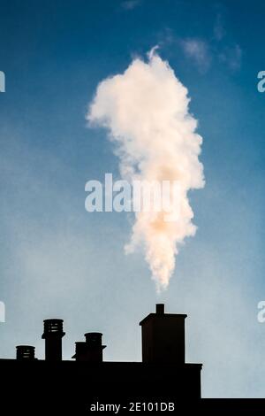 Weißer Rauch aus einem Kamin auf dem Dach eines Wohnhauses. Konzepte von Kälte, Heizung und Verschmutzung Stockfoto