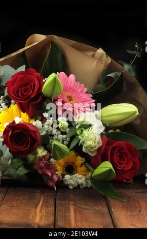 Schöner Strauß von Rosen, Lilien, Gerbera und anderen Blumen und Kräutern. Holzhintergrund. Stockfoto
