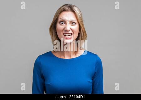 Portrait der schönen emotionalen Frau in engen blauen Kleid stehen mit geballten Zähnen und wütend Grimasse auf dem Gesicht, vorgibt, aggressiv zu sein. Indoor Stockfoto