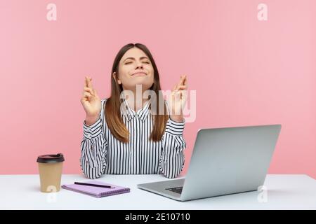 Hoffnungsvolle verträumte Frau Büroangestellte sitzt am Arbeitsplatz in Erwartung der Business-Event, Überkreuzen ihre Finger und wünschen viel Glück, träumen von Stockfoto