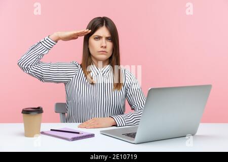 Ja, Sir! Gehorsam verantwortungsvolle Geschäftsfrau sitzen am Arbeitsplatz mit Laptop und salutieren, hören Chef Auftrag, Unternehmensdisziplin. Stehbolzen für den Innenbereich Stockfoto