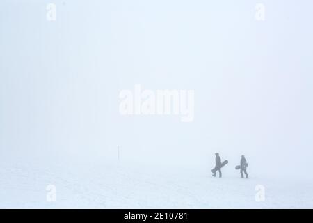Oberried, Deutschland. Januar 2021. Zwei Snowboarder wandern im dichten Nebel nahe dem Gipfel des Schauinslands durch die verschneite Landschaft. Viele nutzen den letzten Tag des langen Neujahrswochenendes für einen Ausflug in den verschneiten Schwarzwald. Quelle: Philipp von Ditfurth/dpa/Alamy Live News Stockfoto