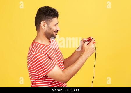 Profil Porträt bärtige Mann in rot gestreiften T-Shirt halten in Händen rot Gamepad Joystick, Grimacing spielen Videospiele. Innenaufnahme des Studios isoliert Stockfoto