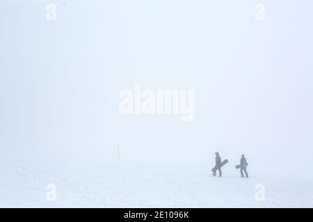 Oberried, Deutschland. Januar 2021. Zwei Snowboarder wandern im dichten Nebel nahe dem Gipfel des Schauinslands durch die verschneite Landschaft. Viele nutzen den letzten Tag des langen Neujahrswochenendes für einen Ausflug in den verschneiten Schwarzwald. Quelle: Philipp von Ditfurth/dpa/Alamy Live News Stockfoto