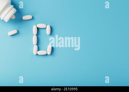 Der Buchstabe des Vitamins C in den Kapseln gießen aus dem Glas auf einem blauen Hintergrund aus. Freier Speicherplatz Stockfoto