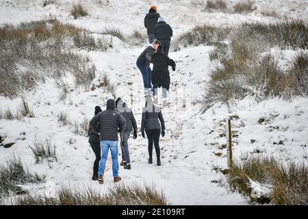 Wanderer helfen sich gegenseitig, den Pfad zum Gipfel des Pen y Fan, dem höchsten Berg von Südwales, bei schneebedeckten Bedingungen zu besteigen. Stockfoto