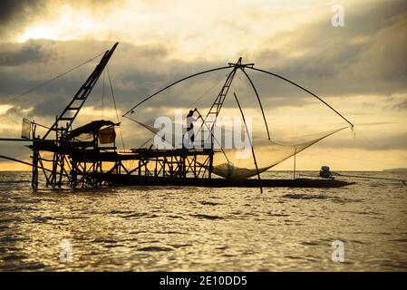 Silhouette eines Fischers, der an einem riesigen quadratischen Fischnetz in Pakpra, Provinz Phtthalung, Thailand arbeitet. Stockfoto