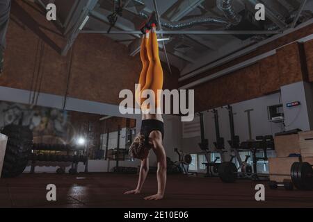 Ganzkörperaufnahme einer Sportlerin, die im Fitnessstudio der Crossfit-Box den Handstand macht. Athletische Frau, die auf ihren Händen im Fitnessstudio läuft, Platz kopieren. CrossFit, Balance c Stockfoto