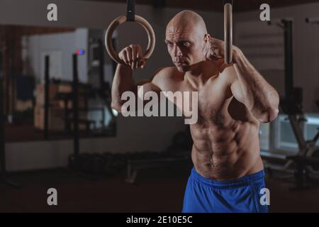 Reifer männlicher Crossfit-Athlet mit starkem muskulösen Körper und perfektem abs, der heftig zur Kamera schaut, nach dem Gymnastikring-Workout ruht, Copy Spa Stockfoto