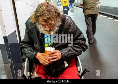 Berlin, Deutschland. Älterer Erwachsener Obdachloser Mann in einem Rollstuhl bettelt um Geldfetzen in der U-Bahn-Station Schonleinstraße. Stockfoto