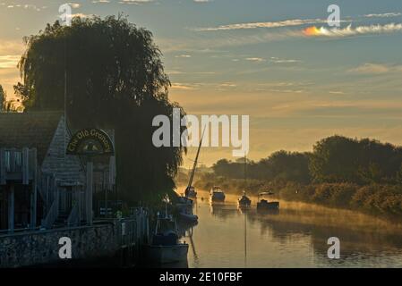 Blick auf einen Sonnenaufgang und Sonnenhunde über dem River Frome und dem Wareham Quay von South Bridge, Wareham, Dorset, England, UK an einem hellen nebligen Morgen. Stockfoto