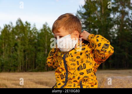 Ein Junge in einer gelben Jacke zieht einen Arzt an Maske an einem hellen sonnigen Tag Stockfoto