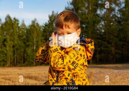 Ein Junge in einer gelben Jacke zieht einen Arzt an Maske an einem hellen sonnigen Tag Stockfoto