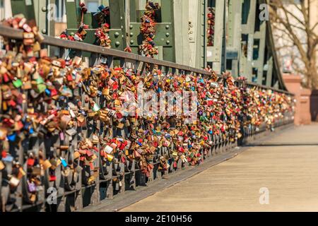 Viele Schleusen auf dem grünen Brückengeländer der Eisenbrücke in Frankfurt über dem Main. Liebesschlösser in verschiedenen Farben im Sonnenschein. Stockfoto