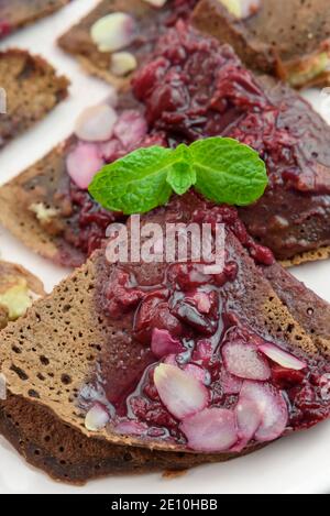 Schokolade vegan, glutenfreie französische Pfannkuchen (Crepes) mit Hirsefüllung und Fruchtsauce mit Mandeln, 45 Grad Nahaufnahme, fröhlich, helle Farben, hoch Stockfoto
