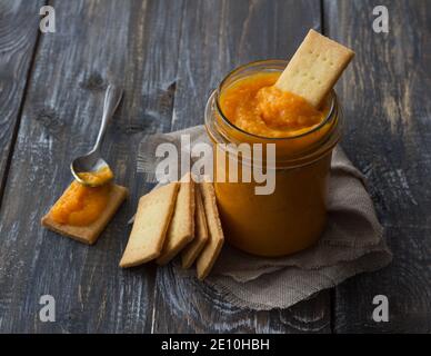 Gesunde rohe Orangenmarmelade mit getrockneten Aprikosen in einem Glas mit Cookies auf einem Holztisch. Diät-Essen. Selektiver Fokus. Rustikaler Stil Stockfoto