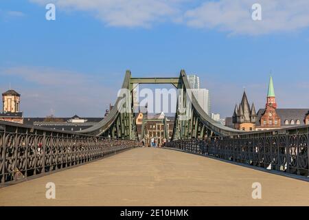 Fußgängerbrücke über den Main in Frankfurt. Eisenbrücke tagsüber mit wenigen Leuten. Häuser der Altstadt im Hintergrund mit Sonnenschein Stockfoto