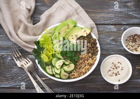 Grüner Salat mit Linsen, Quinoa, Avocado, Gurke, frischem Salat und Gemüse mit Tahini-Sauce. Buddha-Schale. Auf einem hölzernen Hintergrund, Draufsicht Stockfoto