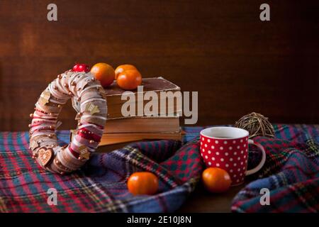 Rot gepunkteter Becher oder Teetasse mit heißer Schokolade auf einer schottischen Decke mit Kranz. Gemütliches Hauskonzept mit Büchern. Eine Tasse festliche heiße Schokolade Stockfoto