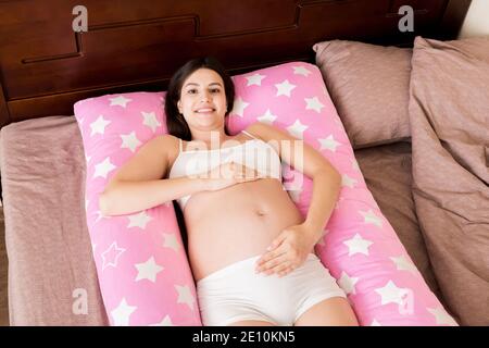Junge schwangere Frau liegt im Bett mit unterstützendem Kissen. Stockfoto