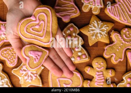 Zwei Herzkekse mit Dekoration zum Valentinstag in Frauenhand auf dem Hintergrund von Lebkuchen auf dem Holztisch. Stockfoto