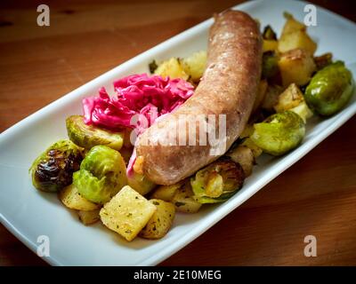 Ungarische Kolbasz-Wurst mit Rosenkohl, Kartoffeln und eingelegtem Kohl auf weißem Teller, Closeup Stockfoto