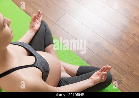 Schöne junge schwangere Frau sitzt auf Matte in Yoga-Pose zu Hause. Schwangerschaft Yoga und Fitness-Konzept bei Coronavirus Zeit. Stockfoto