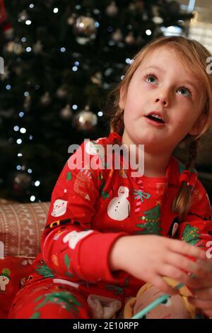 Ein Kind in ihrem Schlafanzug öffnet ihre Geschenke am Weihnachtstag. Stockfoto