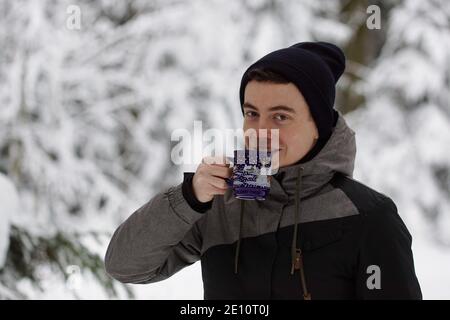 Winter Time - Mann im Schnee, trinken ein heißes Getränk. Hält eine Tasse Tee oder Glühwein vor seinem Mund. Stockfoto