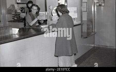 1947, historisch, stehend am Schalter eines Reisebüros oder Ticketbüros, eine Dame, die ein kleines Paket schickt, USA Stockfoto