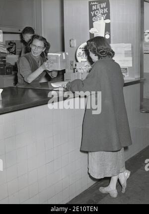 1947, historisch, stehend am Schalter eines Reisebüros oder Ticketbüros, eine Dame, die ein kleines Paket schickt, USA Stockfoto