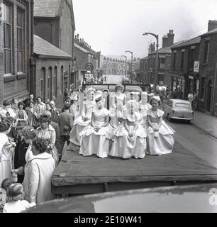 In den 1950er Jahren, historisch, auf der Rückseite eines Lastwagens, der eine Straße entlang fährt, sitzen die May Queen und ihr Gefolge in ihren Kleidern, Farnworth, Lancashire, England, Großbritannien. Der Tag der Rosenkönigin war ein besonderer Tag für die Kinder der Stadt, die an der Sonntagsschule der Kirche teilnahmen und mit der traditionellen "Sommersonnenwende" verbunden waren, die ihren Ursprung in den alten heidnischen Festen hatte. Es wurde manchmal zusammen mit dem Walking Day getan, wenn die Kinder versammelten sich und gingen durch die Straßen. Stockfoto